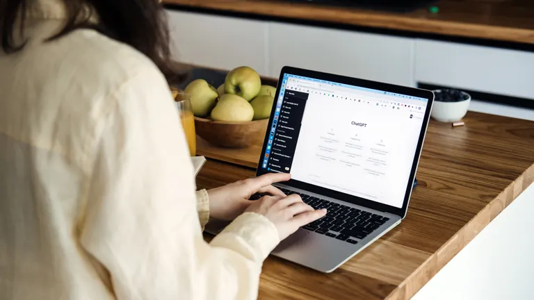 Frau sitzt mit Laptop am Tisch auf dem Laptop sieht man ChatGPT geöffnet